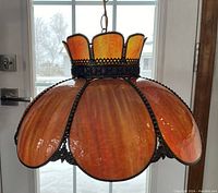 Front view of the vintage burnt orange stained glass lamp hanging with metal chain in front of window.