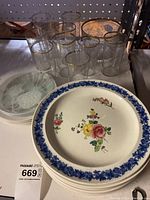 Set of Wedgewood plates stacked with floral design and blue border, accompanied by etched drinking glasses with gold rims and a frosted glass bowl or ice bucket.