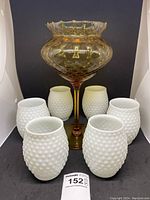 Photo showing Empoli amber diamond optic vase with six white milk glass hobnail glasses arranged around it.