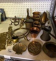 Photo showing a variety of brass and copper decorative pieces, including a Victorian hanging light, shell dish, pitcher, rings, and embossed boxes.