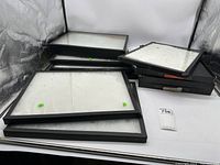 Photo showing a group of black framed display boxes with glass tops and white cotton lined interiors stacked against a backdrop.