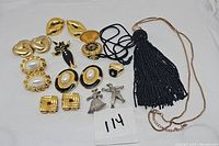 Full assortment of the costume jewelry items including earrings, pins, ring, pocket watch pendant, and black tassel necklace.