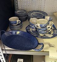 Photo showing Liberty Blue cups stacked on top of dinner plates along with a blue enamel pan with handle.
