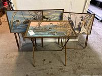Set of 4 folding metal tray tables each with painted duck and bird scenes on tray tops with gold-tone metal legs.