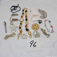 Full view of all jewelry items arranged on white surface with lot number 96, showing assortment of pins, brooches, watches, bracelets, rings, and earrings.