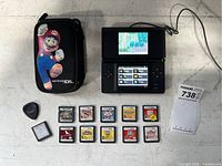 Black Nintendo DS console with Mario-themed case, charger, and multiple game cartridges laid out on a surface.