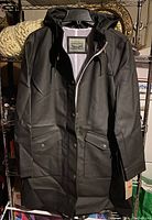 Front view of black Levi's polyurethane rain jacket showing hood, snap button pockets, and partially zipped front with visible label inside.
