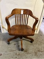 Front view of the solid oak rolling office chair showing slatted wooden backrest and five rolling casters