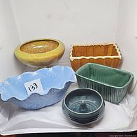 Five pottery planters of varying shapes and glazes arranged together on white tissue paper against wall.