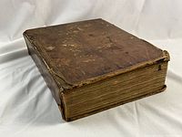 Book closed at an angle showing full brown leather cover with scuffs and worn edges