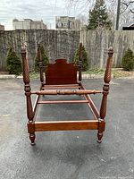 Full view of twin four poster bed made of mahogany with carved posts and headboard at outdoor setting.