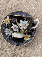 Top view showing the hand-painted daffodils on the black bone china tea cup and matching saucer with gold rims.