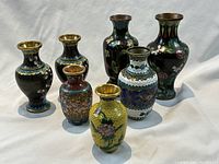 Seven hand-decorated cloisonné vases shown together, displaying variety in size and design.