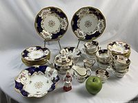 Overall view of collection including teapot, cups, plates, creamers and bowls with green apple for scale