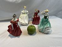 Four Royal Doulton figurines displayed with a green apple for scale