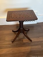 Flip-top wooden side table with detailed wood inlay and four legs with inlay, viewed from front.