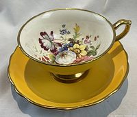 Photo of the tea cup with floral pattern inside and yellow saucer with gold rim, taken from above at an angle.