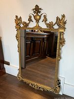 Full view of rectangular mirror leaning against wall, showing overall gilt carved wood frame and mirror surface