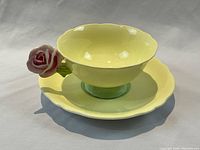 Front view of yellow-green teacup and saucer set showing scalloped edges and pink rose handle