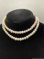 Front view of the pearl necklace displayed doubled on a black bust showing the pearls and clasp.