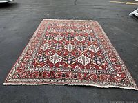 Full view of red Persian area rug laid on asphalt surface.