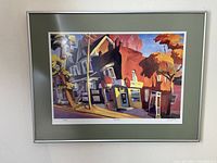 Full view of framed print titled "Variety Store" showing urban street scene with houses and store, in green mat and silver frame.