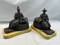 Both seated figurines side by side on light backdrop