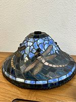 Tiffany style lamp shade on wooden surface showing overall shape and dragonfly motif.