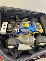 Remote control rock truck with blue flame body inside a black padded carrying case along with some accessories including battery charger and spare tires.