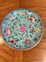 Round Japanese porcelain dish with turquoise background featuring various colorful flowers and butterflies, decorated in Hong Kong.