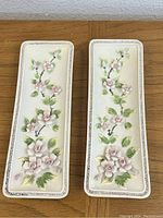 Front view of pair of floral wall art plaques showing raised pink flowers and green leaves on cream background with decorative borders.