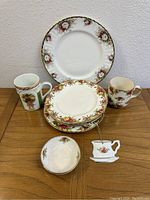 Overview of china set on wooden table showing several plates, bowls, mugs and a teacup-shaped pin, all with floral rose designs and gold trim.