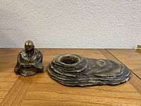 Seated brass Buddha sculpture beside layered brass incense holder on wooden surface.