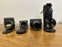 Four lenses lined up with some caps and cases on a wooden surface.