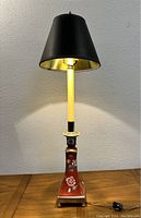 Full view of tall vintage lamp showing ceramic base with floral design, cream stem, and black and gold lampshade.