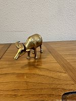 Side view of vintage brass water buffalo figurine on wooden surface against a wall