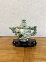 Front view of a green jade pot featuring an ornate dragon carving wrapped around the body, displayed on a wooden stand.