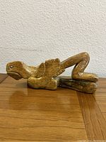 Side view of vintage abstract stone sculpture showing stylized form with bent legs and ribs, lying on a stone base.