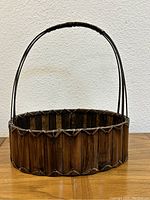 Front and side views of a vintage wooden basket with a rounded handle wrapped near the base.