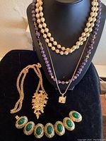 First photo showing necklaces on display bust and chunky bracelet on black surface