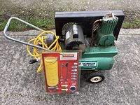 Side view showing the green compressor tank with attached motor and yellow coiled air hose, the Craftsman accessory kit leaning against the compressor.