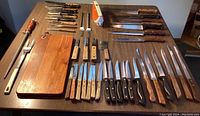 Top down view of the full cutlery lot showing various knives, forks, an electric sharpener, and cutting board on a table.