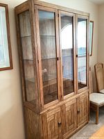 Front and angled view showing entire Drexel wooden hutch display cabinet with glass front doors and glass shelves inside.