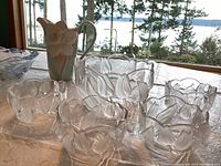 Overview of the ceramic pitcher with a large daffodil flower and multiple clear glass tulip-embossed serving dishes on a table with outdoor background
