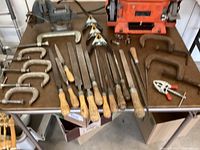 Photo showing 8 metal files with wooden handles, 6 metal C-clamps, and 2 pairs of spring clamps on a table.