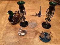 View of all items including two green and clear glass candle holders, a large glass duck, a blue glass base with swans, a clear glass swan, and a hummingbird on a clear base.