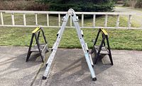 Photo showing the long extension ladder laid horizontally on two plastic sawhorses and the fold-up aluminum ladder standing upright.