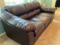 Front angle view of brown leather sofa with three seat cushions and padded arms.