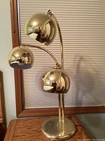 Photo showing full front view of the gold table lamp with three spherical lampshades and round base.