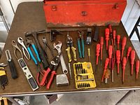 Photo of assortment of hand tools laid out beside toolbox, including pliers, screwdrivers, hammer, wrenches, measuring tape and bit sets